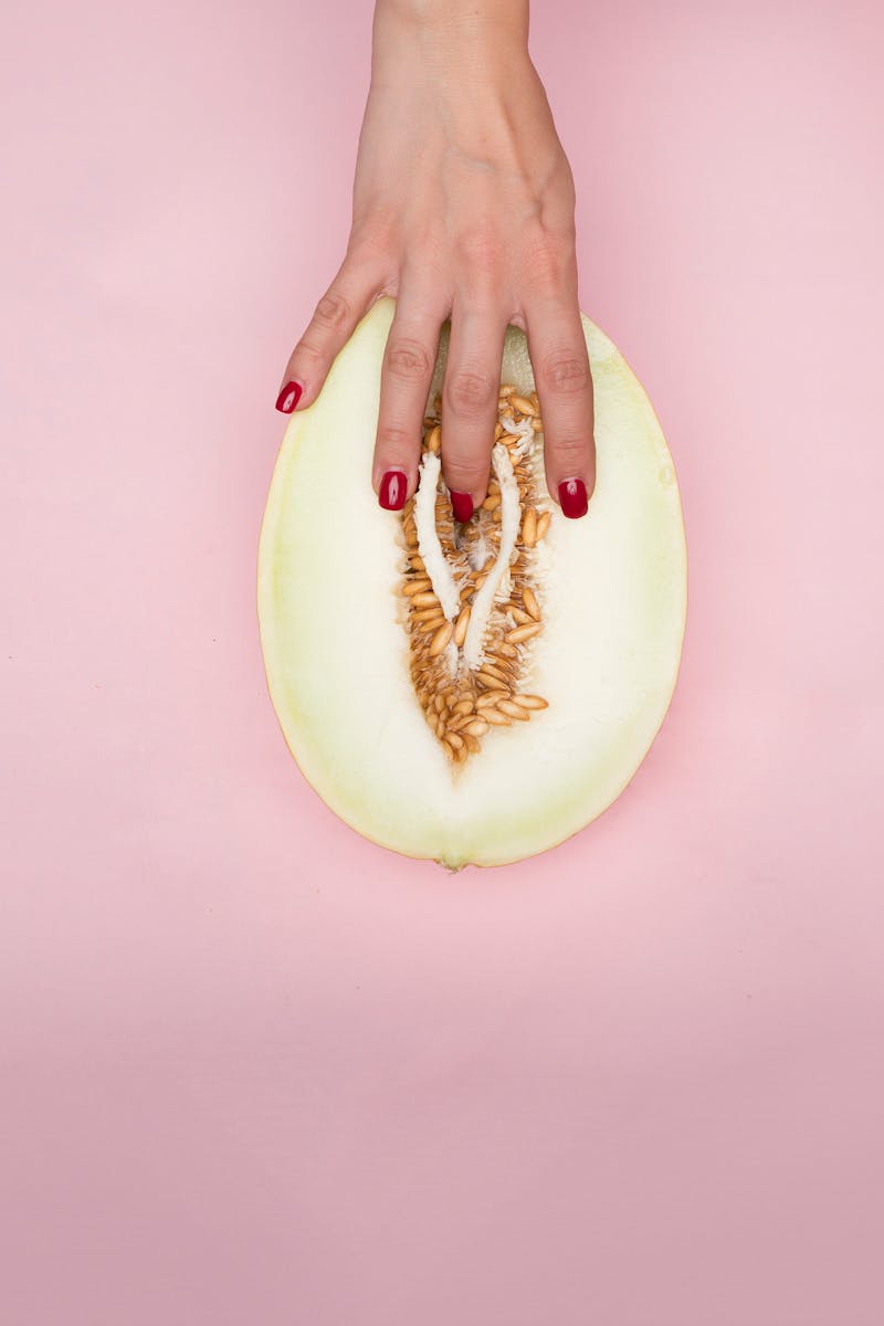 A hand gently touches a melon slice on pink background, emphasizing texture and color.